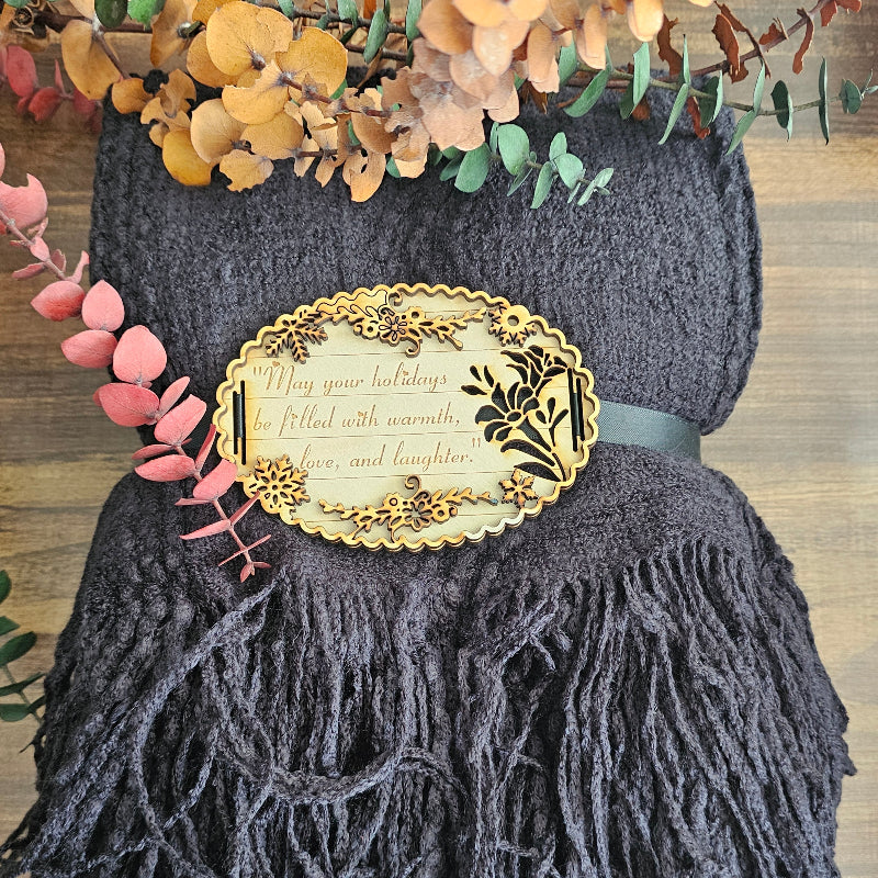 Dark gray yarn with decorative gold tag and tassels on a wooden surface with foliage.