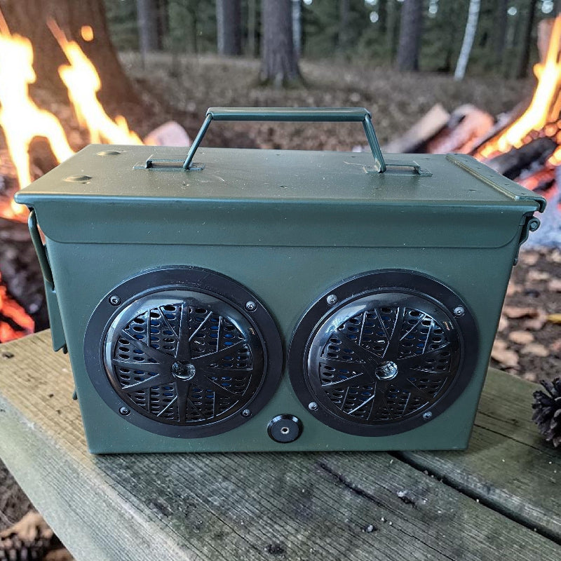 Green metal container with dual circular vents on a wooden surface with a campfire in the background.