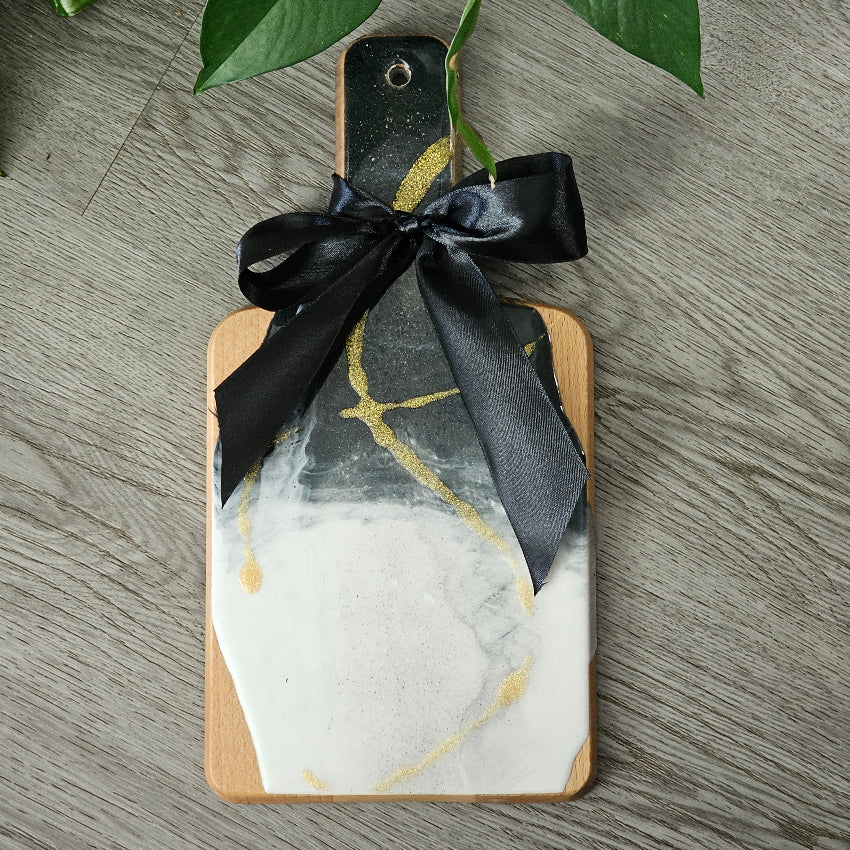 Marble-patterned cutting board with black ribbon on a wooden surface