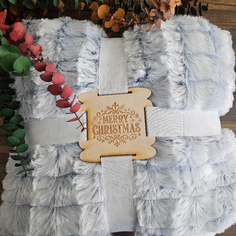 Gray textured blanket with a decorative wooden tag on a wooden surface with foliage.