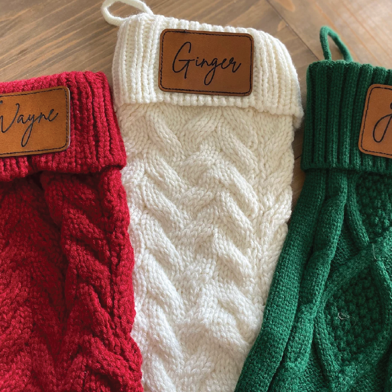 Three knitted items in red, white, and green with leather name tags on a wooden surface.