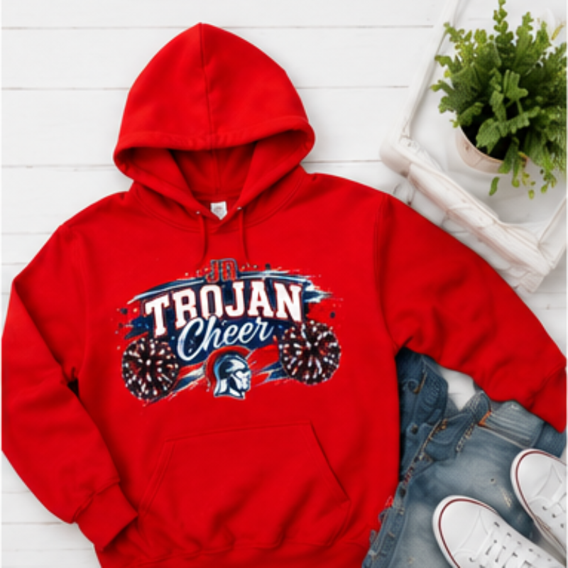 A red pullover hoodie with a 'Trojan Cheer' graphic on the front, styled in a flat lay with blue jeans, white sneakers, and a small potted plant on a white wood plank background.
