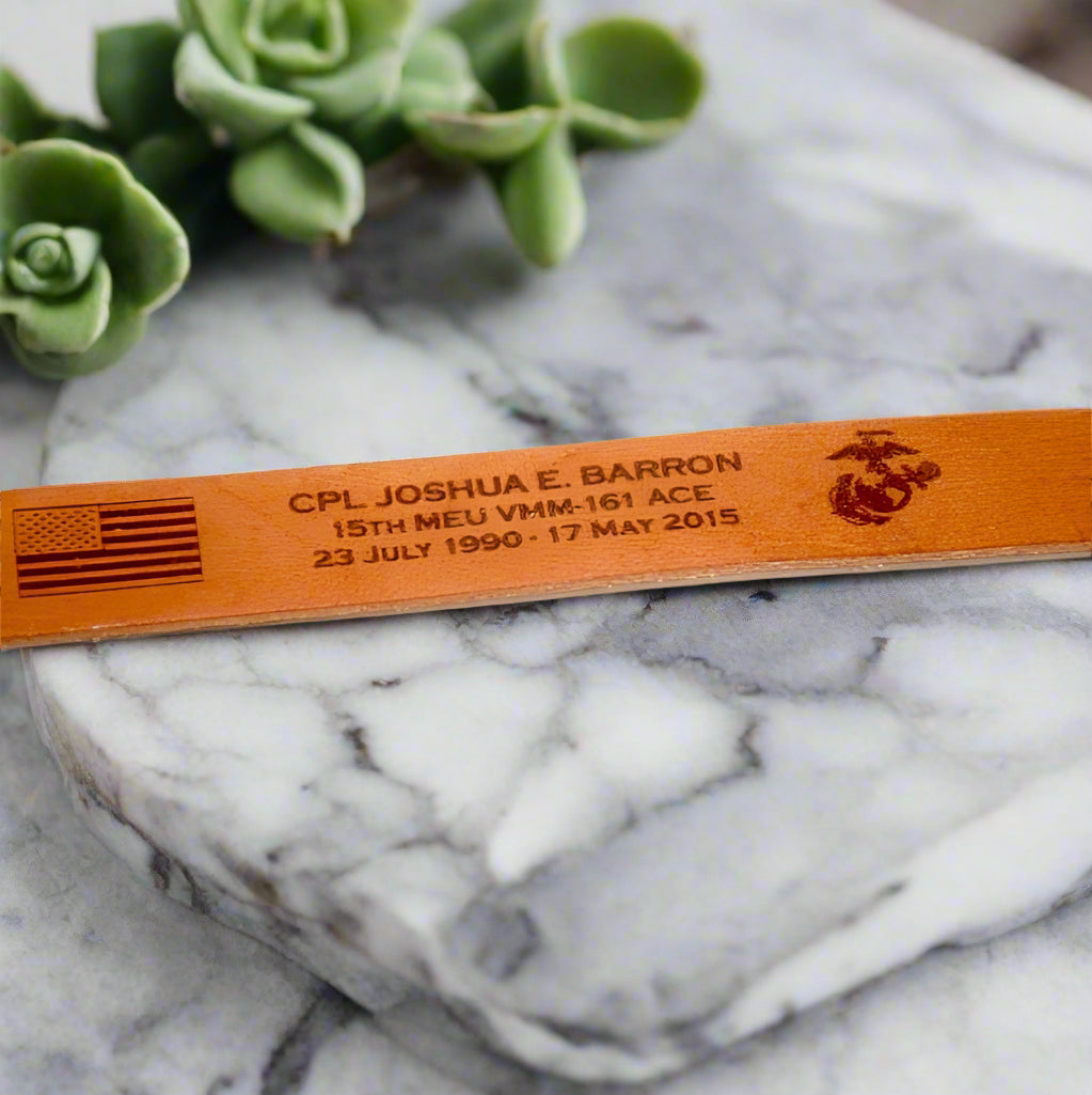 Brown leather memorial bracelet with engraved text and military logo. 