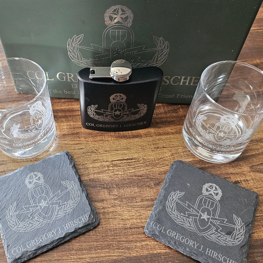 Black flask and two glasses with engraved design on a wooden surface