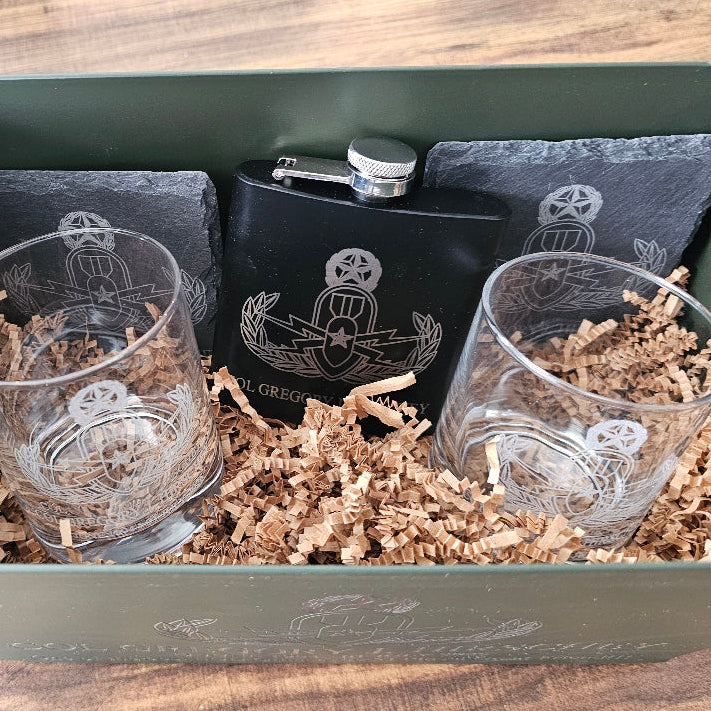 Black flask and two engraved glasses in a decorative box with wooden surface.