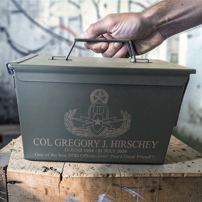 Metal box with engraved text and insignia on a wooden surface