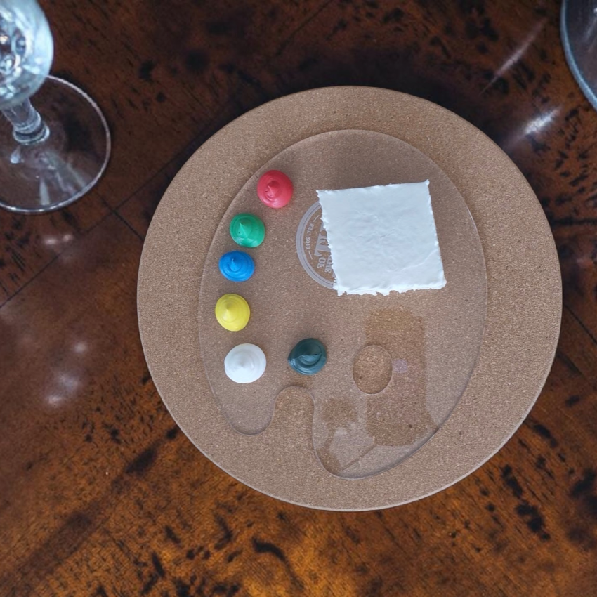 Artistic setup with a palette, paint, and a glass on a wooden surface