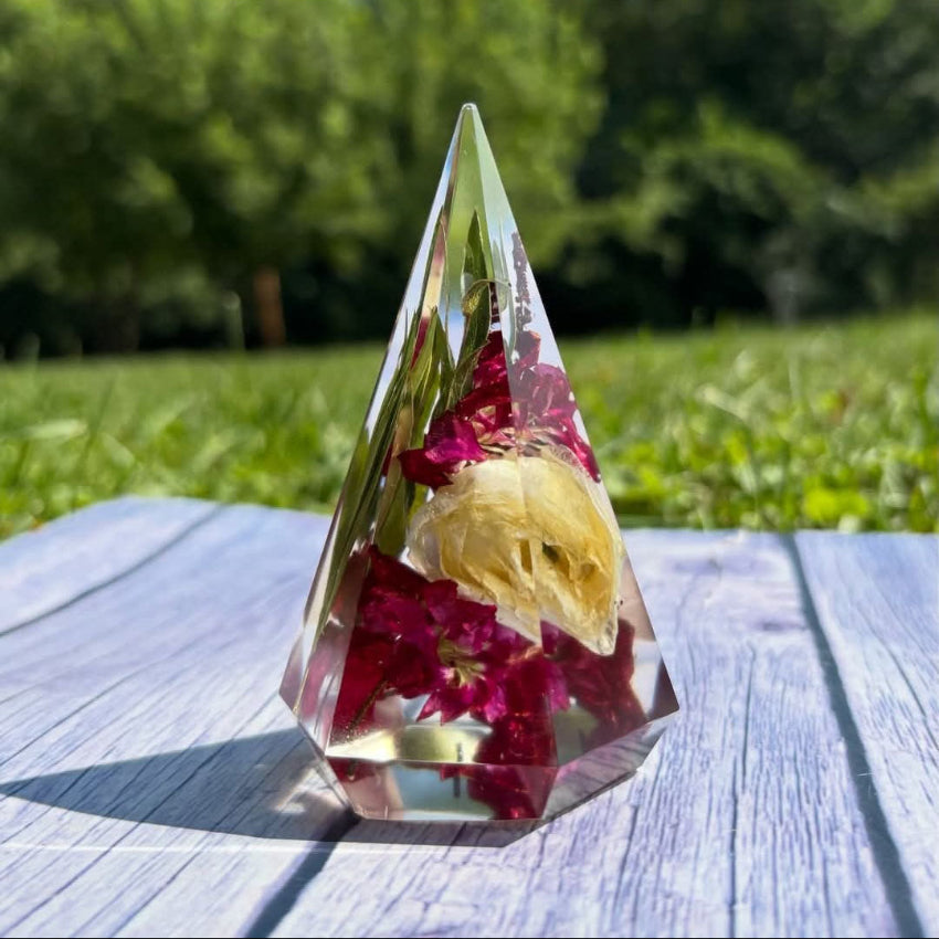 Crystal pyramid with preserved flowers on a wooden surface outdoors