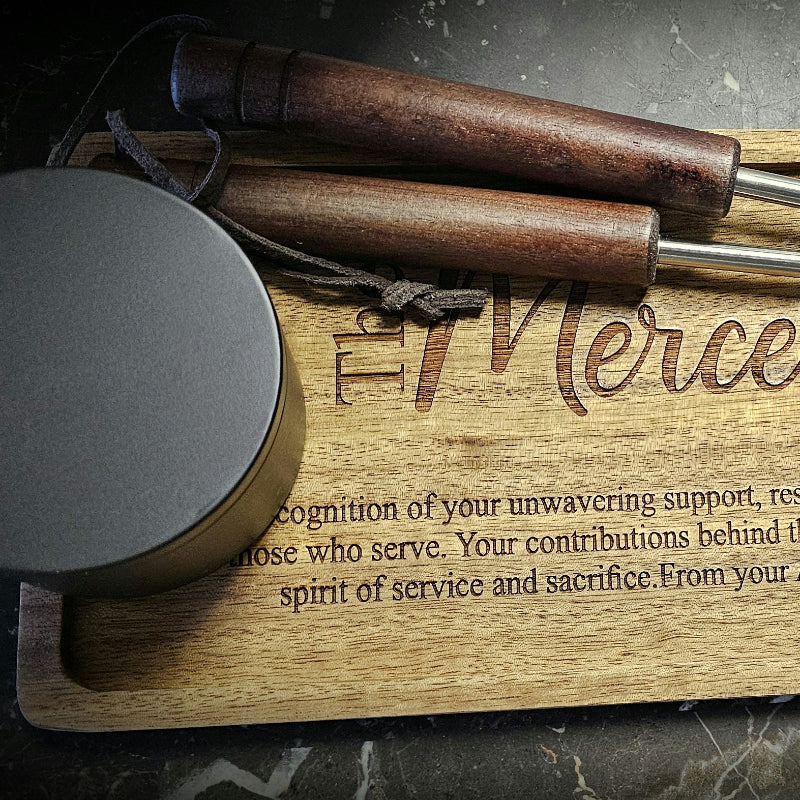 Wooden cutting board with engraved text and metal lid on a dark surface