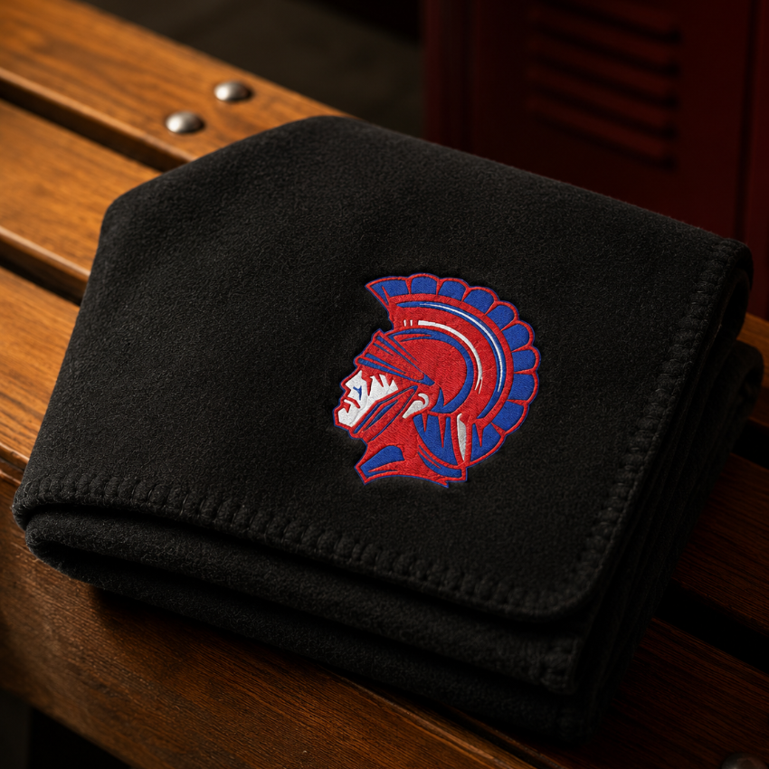 A folded black fleece blanket featuring an embroidered red and blue Spartan helmet logo, resting on a wooden bench.