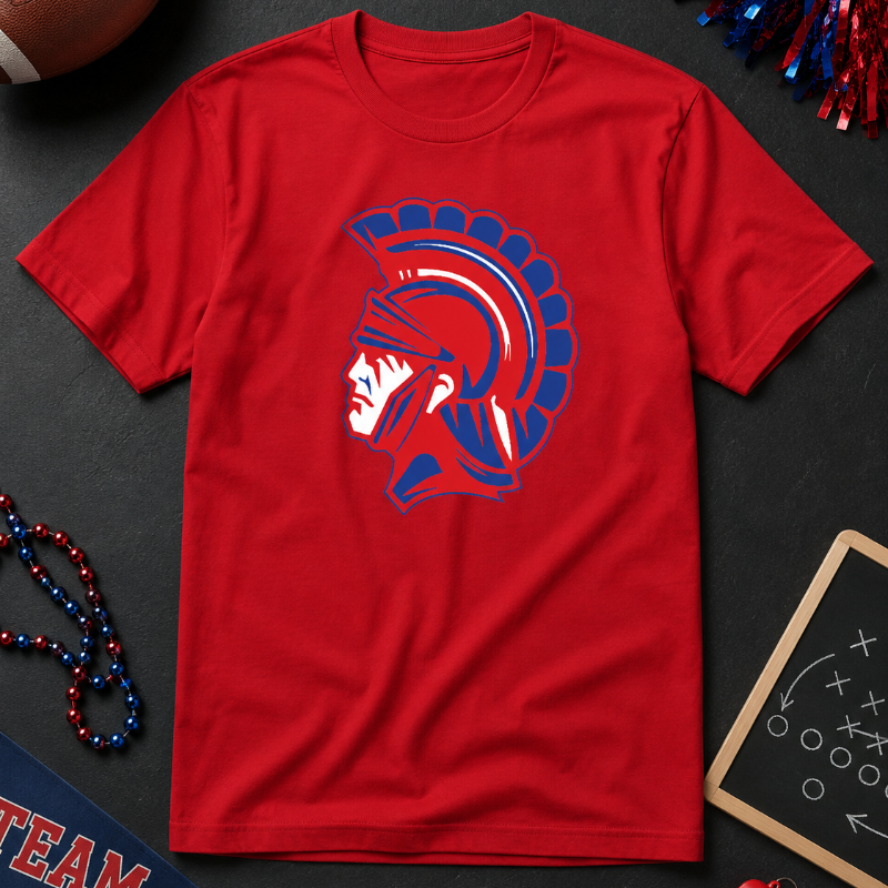A red short-sleeve crewneck t-shirt featuring a blue and white Spartan helmet graphic on the chest, presented in a flat-lay arrangement with sports-themed props like a football, pom-poms, and a chalkboard.