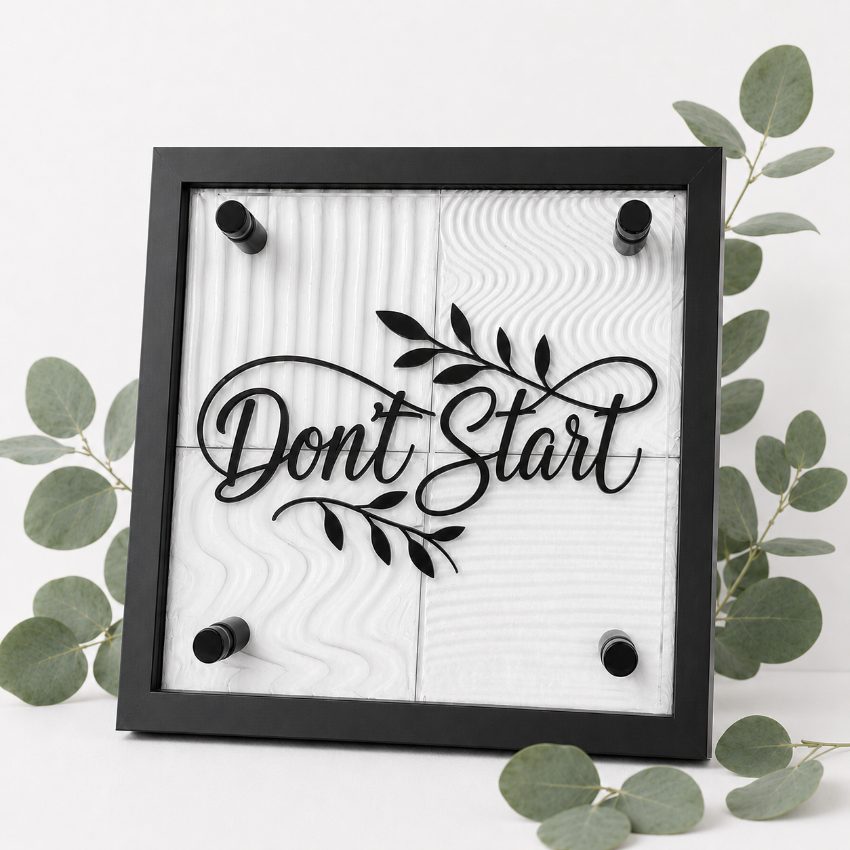 A square black-framed wall sign with the phrase “Don’t Start” in black script over a white textured background, styled with eucalyptus leaves on a light surface.