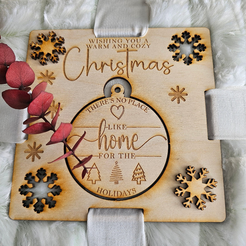 Wooden Christmas ornament with engraved text and snowflake designs on a white fabric background.